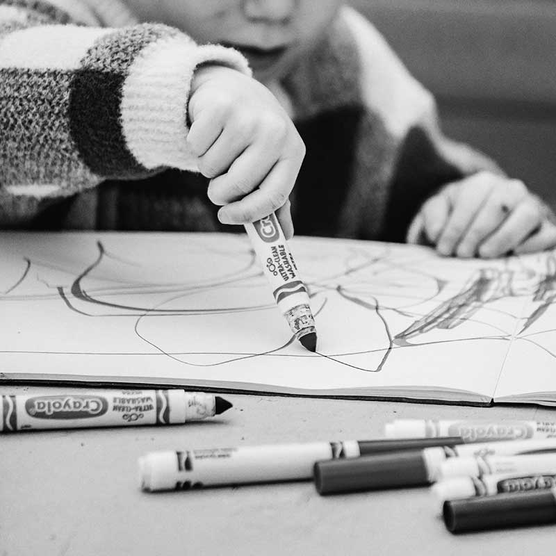 Image en noir et blanc représentant un enfant qui d
dessine avec des feutres