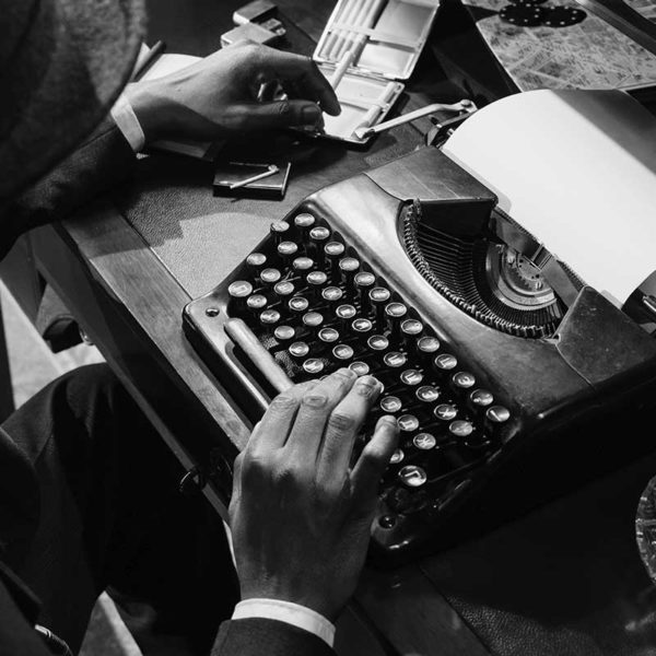 photo en noiret blanc montrant un homme en train de taper à la machine à écrire