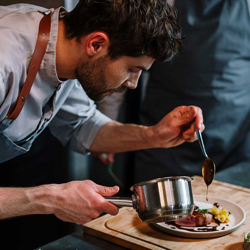 Photo d'un jeune chef cuisinier disposant miticuleusement ses ingrédients dans l'assiette lors du dressage